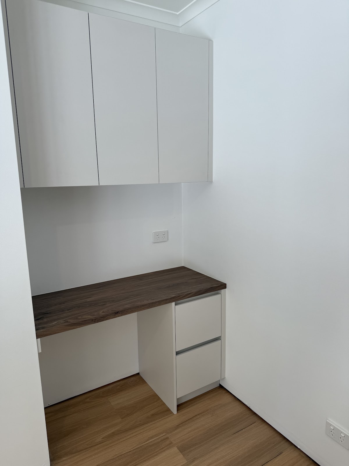 White overhead cupboards above a timber-top study desk and drawer unit
