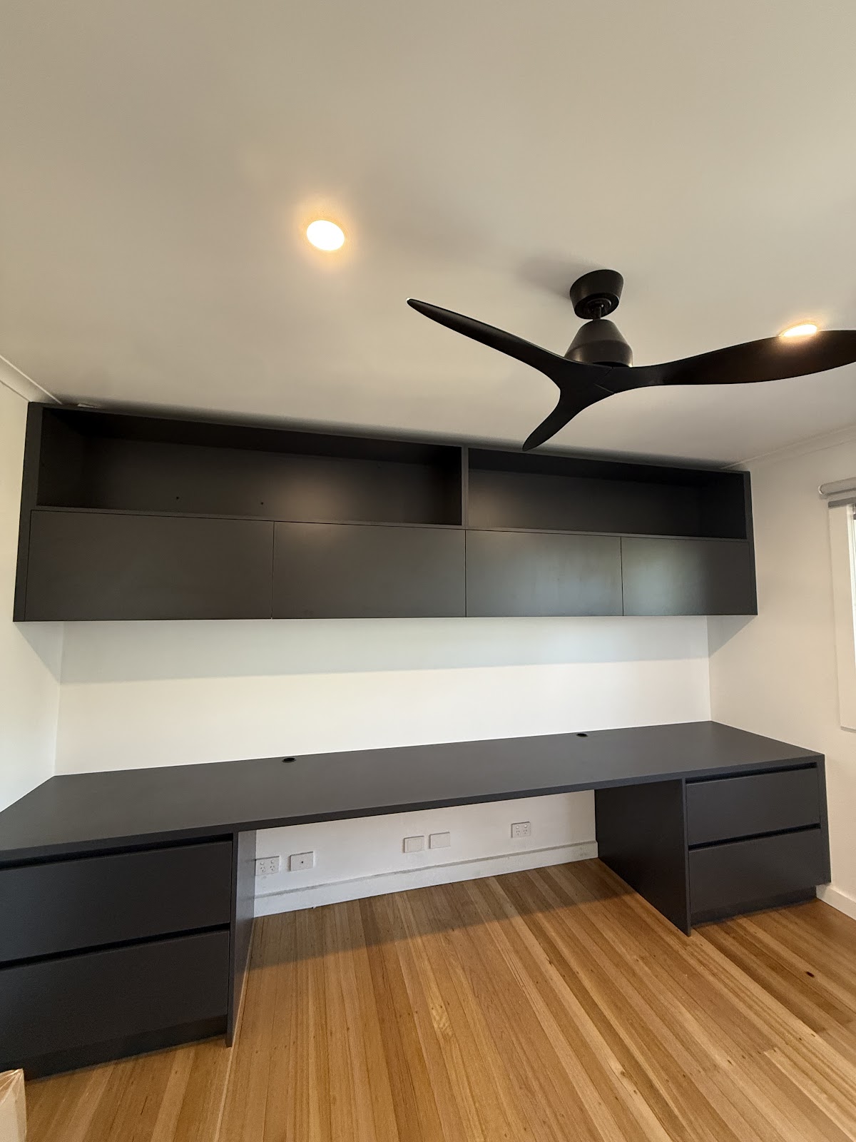 Matte black overhead cabinets above a long black desk with drawers