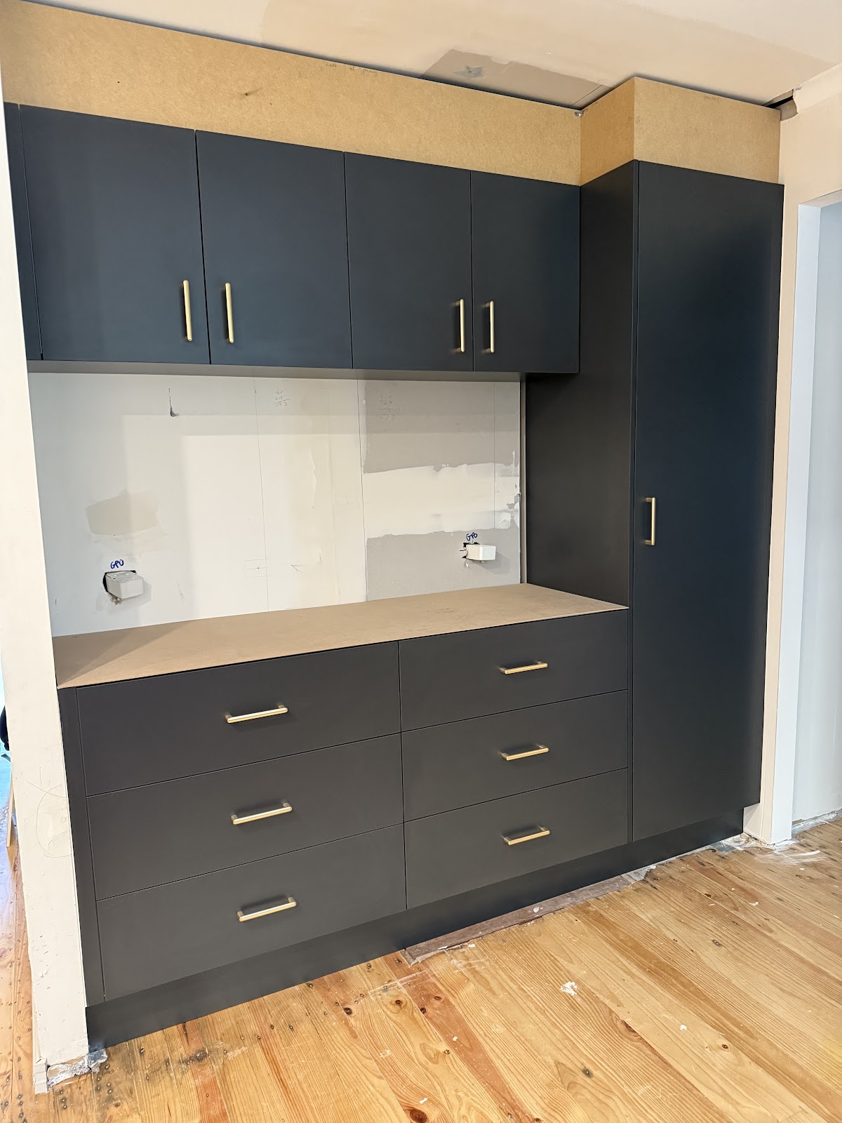 Charcoal full-height cabinetry with brass handles being installed