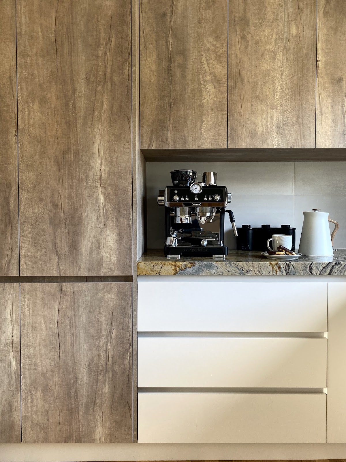 Tall timber-grain cabinets framing a coffee station with a stone benchtop and white drawers