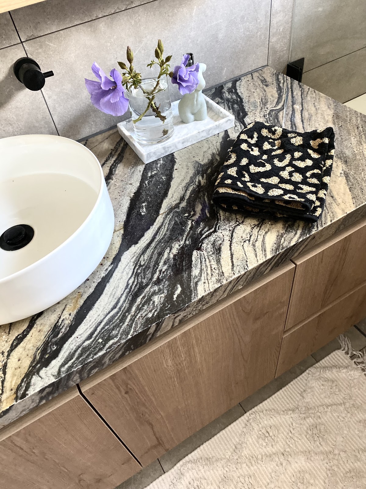 Close-up of a vanity with a dramatic black and gold veined stone top, round white basin and timber-grain drawers